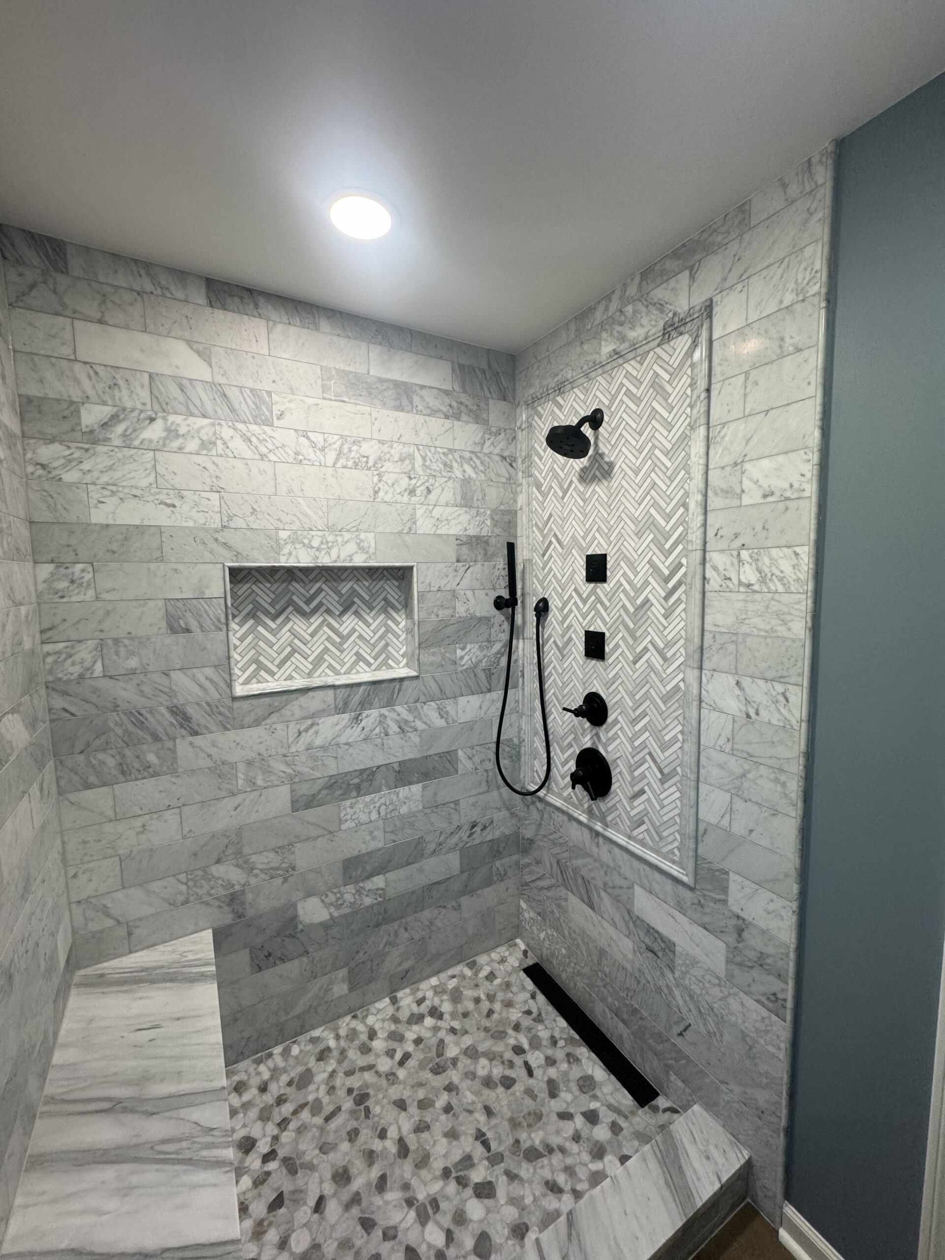 Custom tile shower with glass enclosure and gray stone walls from a bathroom remodel in Bargersville IN by Insta Pro Construction.